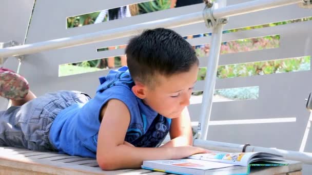 A fiú könyvet olvas a parkban a padon..