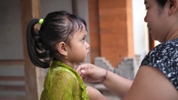 妈妈在巴厘岛的宗教庆典前帮小女孩穿衣服 漂亮的孩子穿着妈妈的衣服 靠近点 — 图库视频影像