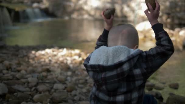 一个小男孩把两块石头扔进森林里的一条小溪里 — 图库视频影像