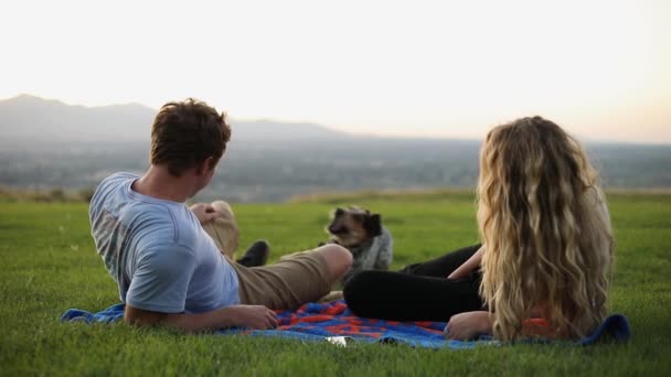 かわいい彼氏とガールフレンドのショット毛布の上に横たわって 彼らのペット犬と遊んでいる間 草の上にピクニックを持っている — ストック動画