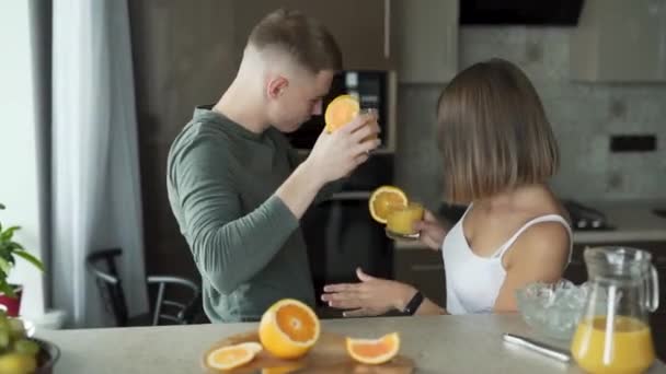 Fiatal pár táncol, miközben narancslevet iszik a konyhapult mellett.