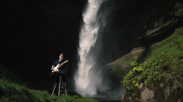 Muž hrající na kytaru před krásným vodopádem na Islandu. SlowMo a záběry v reálném čase od Sony a7iii a Ronin S.