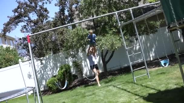 遅い動きショットの女の子の遊び場でスイングに彼女の弟をプッシュ彼らの裏庭で — ストック動画