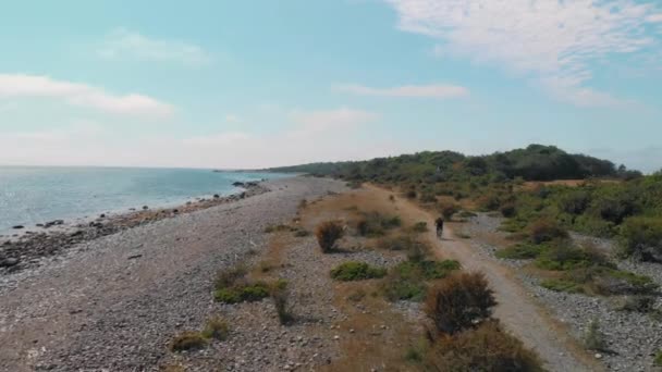 人们骑着自行车 沿着海边的石滩 在美丽的风景中骑车 空中4K — 图库视频影像