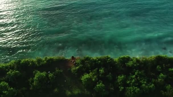 スローモーションの空中パン 崖の上に立つ少女 夕日の波で豪華な海を見下ろすバリ島4K — ストック動画