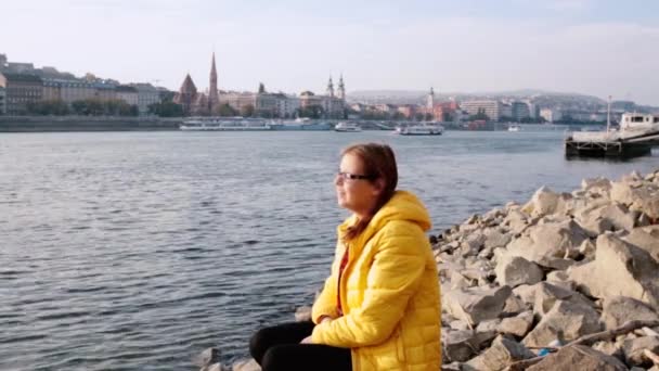 Young Woman Wearing Yellow Jacket Sitting Next Danube River Embankment — Stock Video