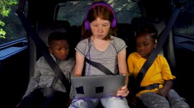 Çocuklar arabanın arka koltuğunda tabletin üzerinde.