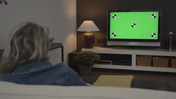緑の画面のクロマキーオプションと現代のリビングルームでテレビを見て若い女性のワイドショットVfx — ストック動画