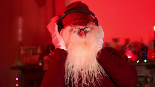サンタはヘッドフォンとダンスを通して音楽を聴く 赤で照らされた部屋 — ストック動画