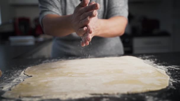 カウンターに広がる生地の上に手をこすり女性 小麦粉は切り分けのために展開ペストリーに落ちる ベーキング中に台所で小麦粉を拭き取る手のスローモーションビュー — ストック動画