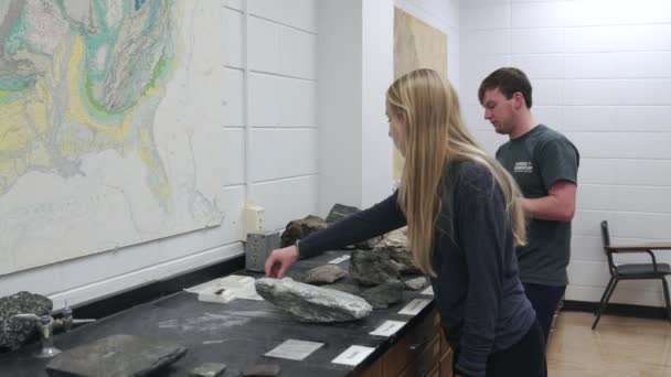 Fiatal nő és férfi Vizsgáló és megvitatása sziklák és ásványi anyagok a munka pad egy fényes geológia osztályteremben belül a nap folyamán