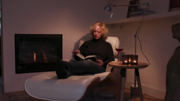 暖炉のそばに座って本を読んでいる女性 — ストック動画
