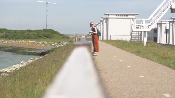 Sarışın Güneş Gözlüklü Turuncu Pantolonlu Asfalt Pantolonlu Bir Kadın Elinde — Stok video