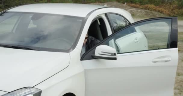 Modny Młody Mężczyzna Skórzanej Kurtce Dostaje Biały Samochód Las Tło — Wideo stockowe