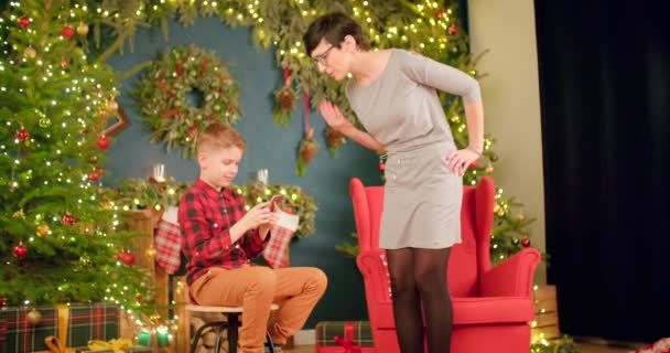 Zoon Naast Kerstboom Speelt Aan Telefoon Terwijl Zijn Moeder Hem — Stockvideo