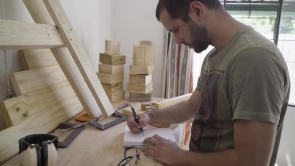Joven Carpintero Masculino Planea Dibujar Proyecto Cuaderno Bocetos Mesa Trabajo — Vídeo de stock