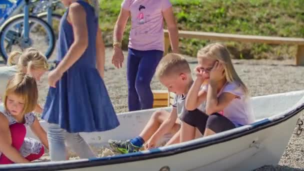 Group of children sitting in a boat which is on land in a playground, playing together with sand