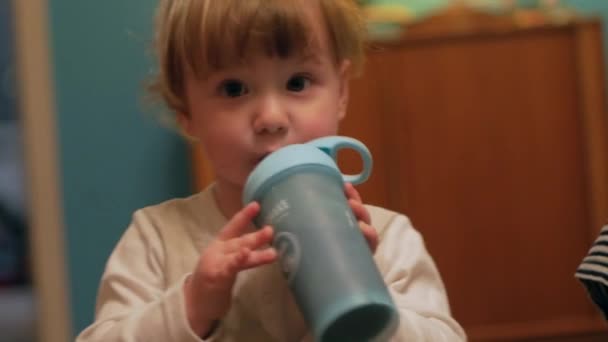 一个英俊的男婴从蓝色的酒瓶里喝着冰沙 仰视着他的父母 — 图库视频影像