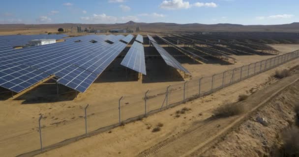 空中ドローン撮影 砂漠の真ん中の土地に太陽光パネルの多くの配列を持つフェンスで囲まれたフィールドに入る 代替グリーンエネルギー生産 — ストック動画
