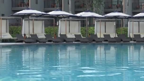 旅行休暇のコンセプトのためのホテルリゾートの屋外スイミングプールの周りの傘とプールベッド — ストック動画
