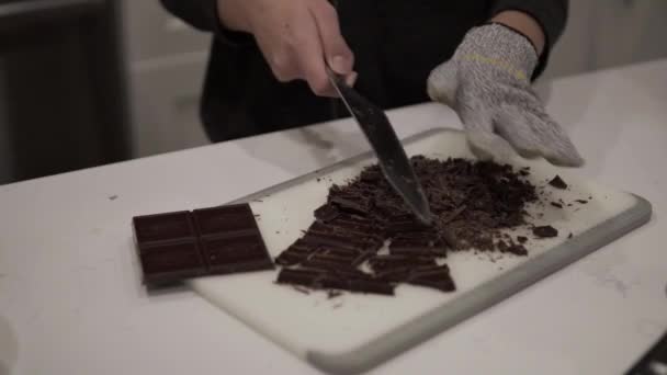 Mladá dívka krájí tmavou čokoládu před tavením pro milionáře sušenky, zatímco na sobě bezpečnostní rukavice