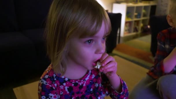 一个小男孩和一个小女孩看电视 吃小吃 — 图库视频影像