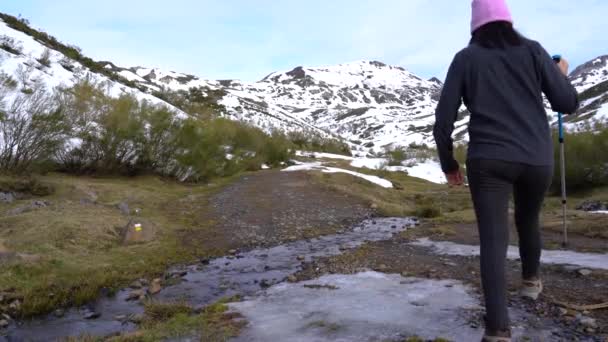 Egy nő átkel egy jeges patakon a hegyekben, miközben túrázik..