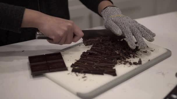 Mladá dívka krájí tmavou čokoládu před tavením pro milionáře sušenky, zatímco na sobě bezpečnostní rukavice