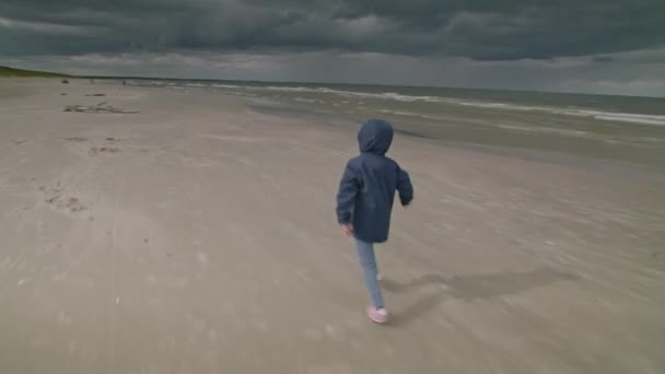 Kleines Mädchen Mit Kapuze Läuft Schnell Strand Einem Bewölkten Stürmisch — Stockvideo