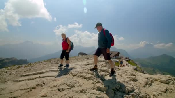 暖かい晴れた日に美しい風光明媚な山の中でバックパックで歩く高齢者の白人夫婦 ドロマイト イタリア Prores — ストック動画