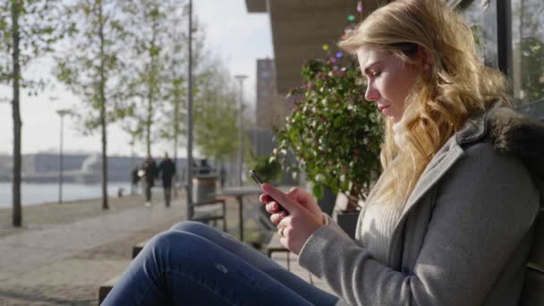 Giovane Donna Utilizza Suo Smartphone Seduto Una Panchina Pubblica Sole — Video Stock