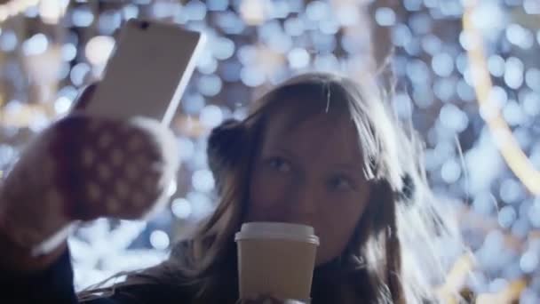 穿着冬衣的快乐的光彩夺目的女人试图点击一个自拍的小杯咖啡 — 图库视频影像