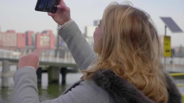 楽しい若い観光客の女性は彼女のスマートフォンで都市のスカイラインの写真を撮ります パララックスを閉じるショット — ストック動画