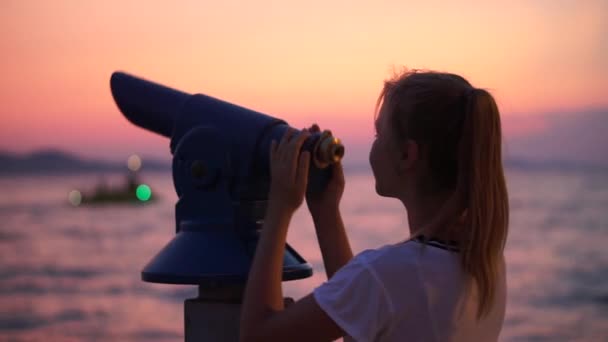 Egy gyönyörű fiatal nő nézi az eget egy fém teleszkóppal a parton naplemente alatt - közelkép lövés
