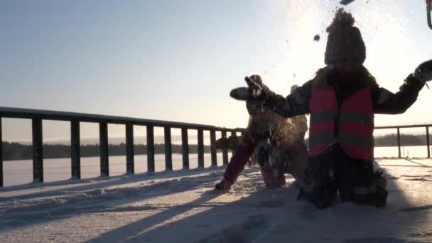 Két aranyos fiatal lány játszik a hóban, nézi a kamera, napsütéses nap, statikus alacsony szög
