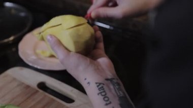 Kollarında dövme olan bir adam keskin kırmızı bir bıçakla bir parça mango dilimliyor. Yakın çekim.
