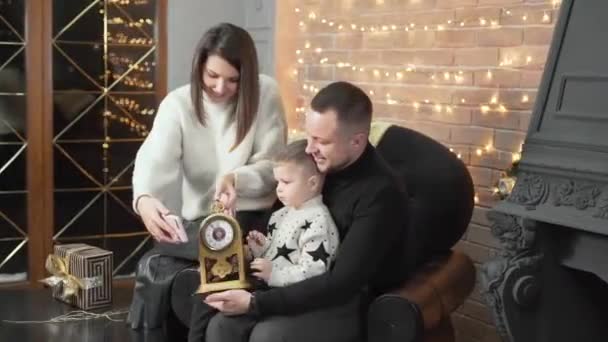 可爱的家人在新年前在家里准备了一棵圣诞树 年轻的母亲 父亲和他们的小儿子坐在椅子上 一边聊天一边看电话里的视频 — 图库视频影像