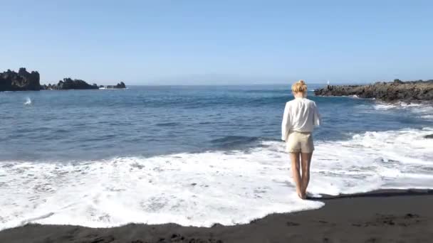 西班牙加那利岛 一个孤独的女人站在海滩上 海浪冲刷着坚尼里菲岛的黑沙海岸 — 图库视频影像