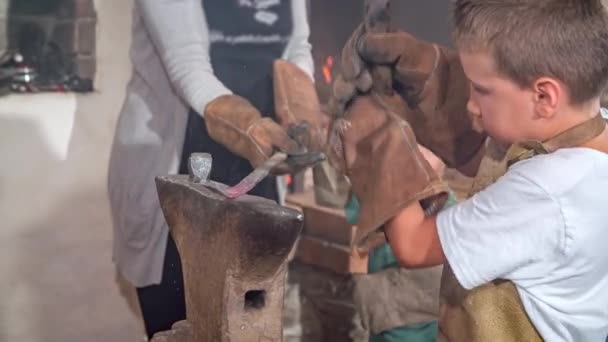 一个小孩一边学习铁匠的工作 一边锤打着一块炽热的红铁 — 图库视频影像