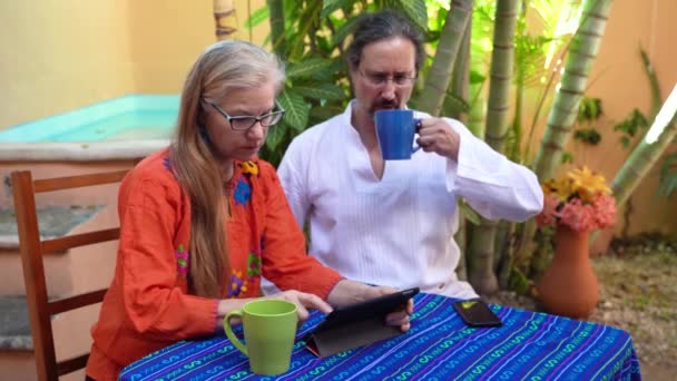 Starší muž pije kávu a žena klepne na tablet počítače venku v zahradě.