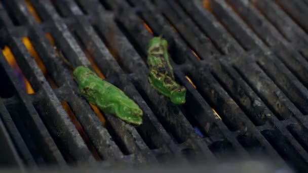 Shishito peppers on a grill in a kitchen are turned over with silver tongs