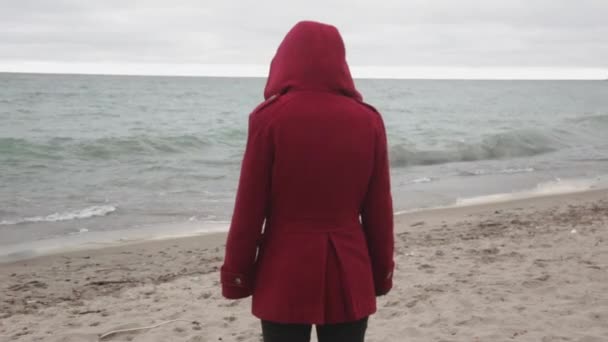 砂浜に立ちながら海の波を見ながら赤いコートを着た人の後ろ姿 クローズアップショット — ストック動画