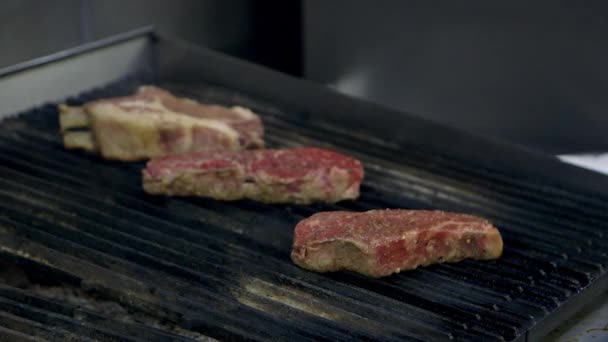 Střední zblízka striptýzových steaků a vepřové kotlety na grilu v kuchyni restaurace.