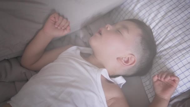 一个身穿夏装 睡在明亮明亮的自然光中的可爱的两岁亚洲男孩的镜头下 慢动作的高角娃娃来回飞舞 — 图库视频影像