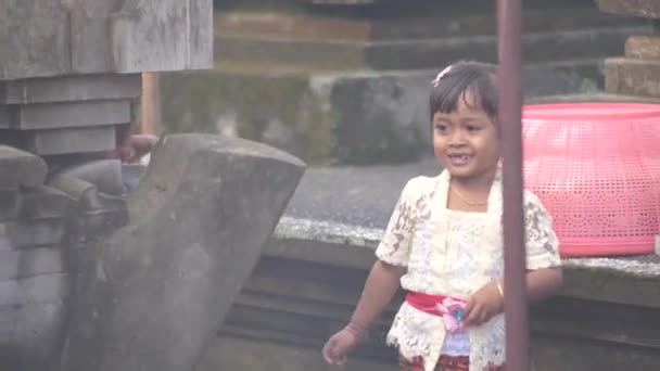 年轻姑娘们在庙宇的院子里玩耍 等待宗教仪式开始 巴厘岛身着传统礼仪服装的漂亮孩子们在烟雾弥漫的纪念碑附近玩耍 — 图库视频影像