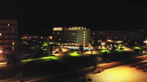 无人机接近一个绿色橙色灯火通明的酒店建筑群 夜间照亮整个环境 — 图库视频影像