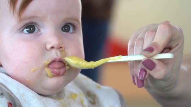 幼児の口の中に赤ちゃんの食べ物の完全なスプーンをヌード母親の手のクローズアップショット その後 幼児は不幸になり それを吐き出し スローモーションで撮影を閉じます — ストック動画