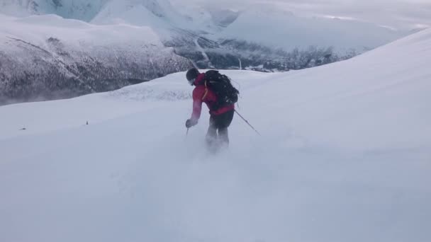 一个身穿红色夹克 滑向下坡 被雪白的山环绕 半明半暗的背景笼罩着云彩的男人的慢镜头 — 图库视频影像