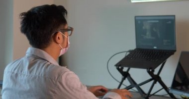 Evde dizüstü bilgisayarla çalışan Coronavirus Asyalı bir adam. Kilitlenme ve kısıtlı hareket emri sonucu uzak çalışma.