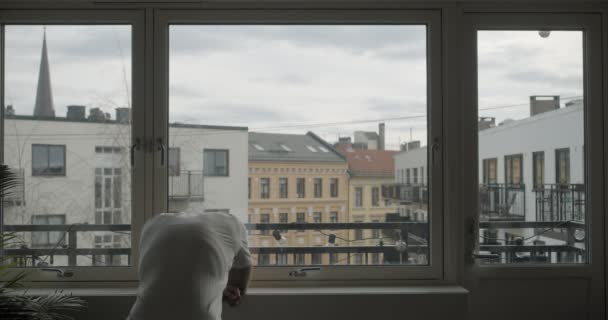 在挪威奥斯陆 一个沮丧的挪威人被隔离在科罗纳病毒检疫室 从有城市背景的黑暗公寓的窗户向外张望 — 图库视频影像